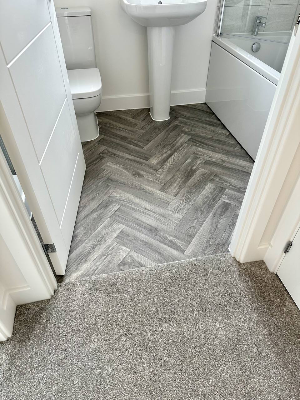 Grey herringbone bathroom floor with carpet at the threshold
