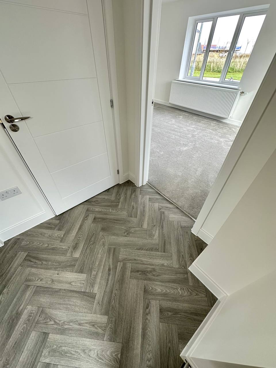 Grey herringbone hallway leading into a carpeted room