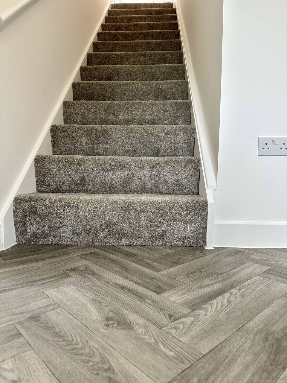 Carpeted staircase meeting a grey herringbone floor
